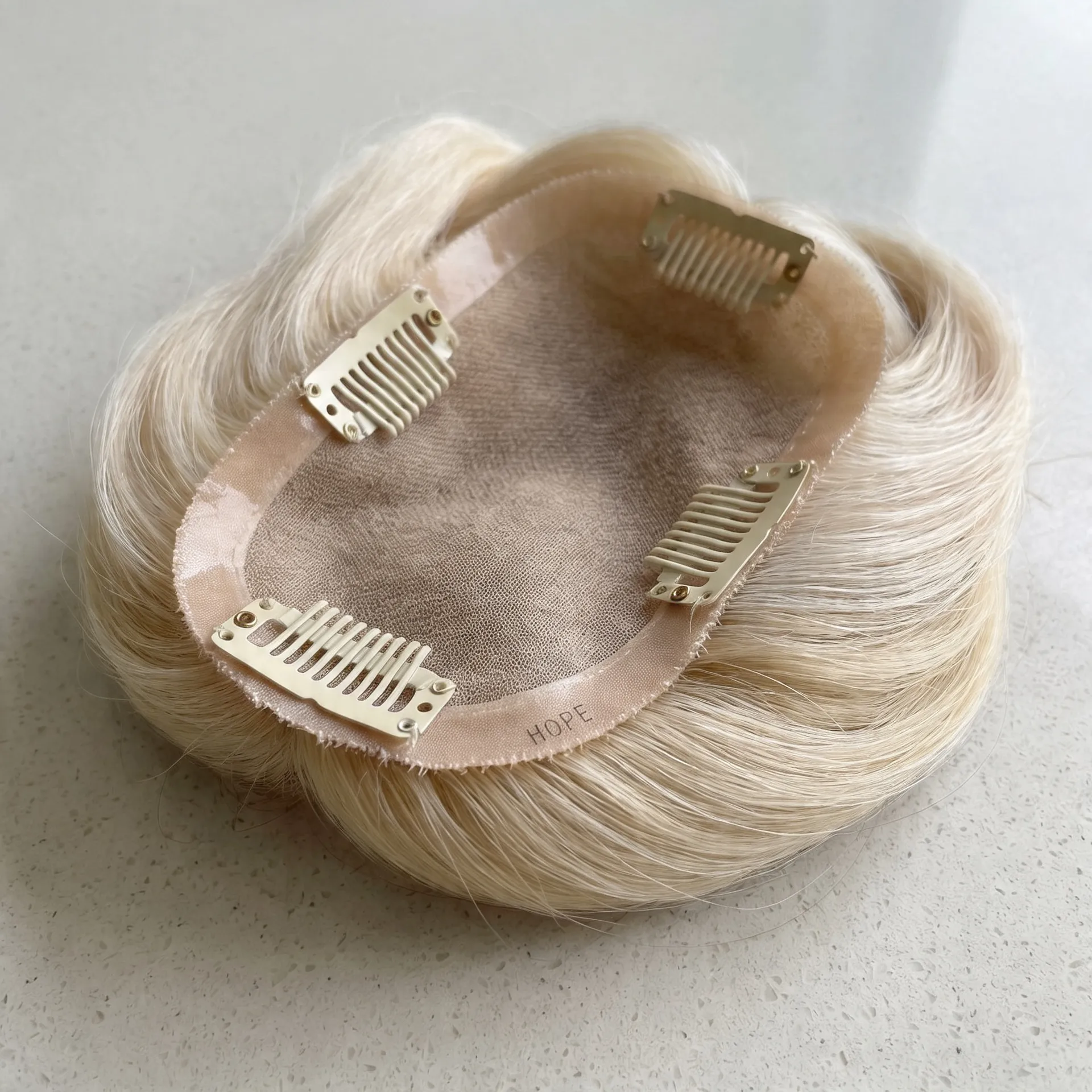 Platinum blonde women's hair topper with monofilament base and gold clip attachments.