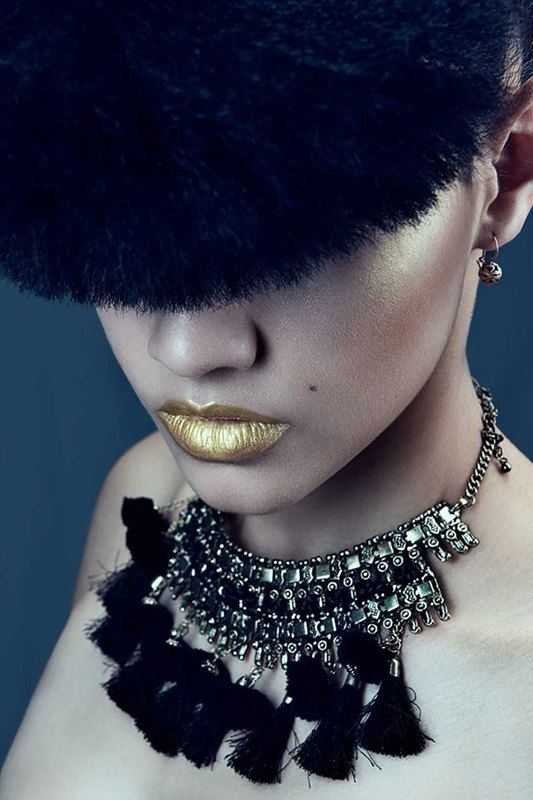 A woman with lustrous gold lip color, a head wear that covers half of her face, and a necklace