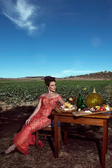 A woman in red gown, on a table set arranged in the middle of a field