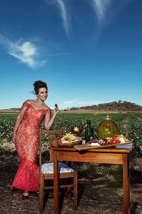 A woman standing beside a table set arranged in the middle of a field