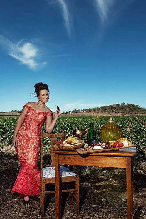 A woman standing beside a table set arranged in the middle of a field