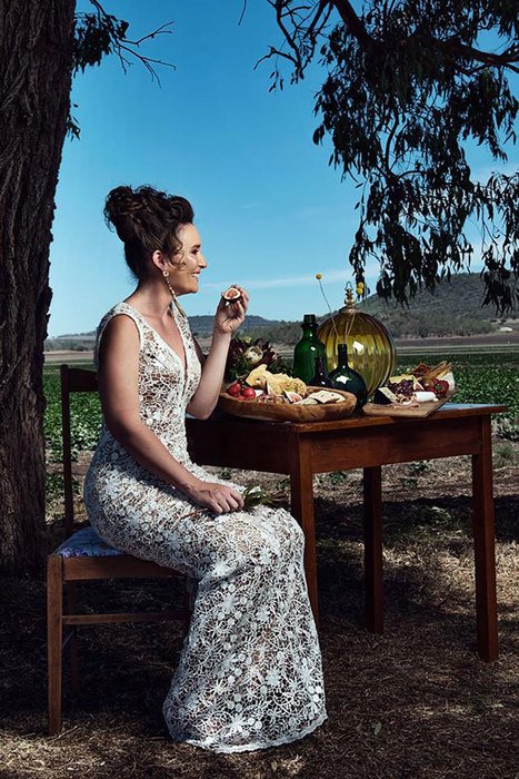 A woman sitting on a chair and posing with fruits under a tree in a field