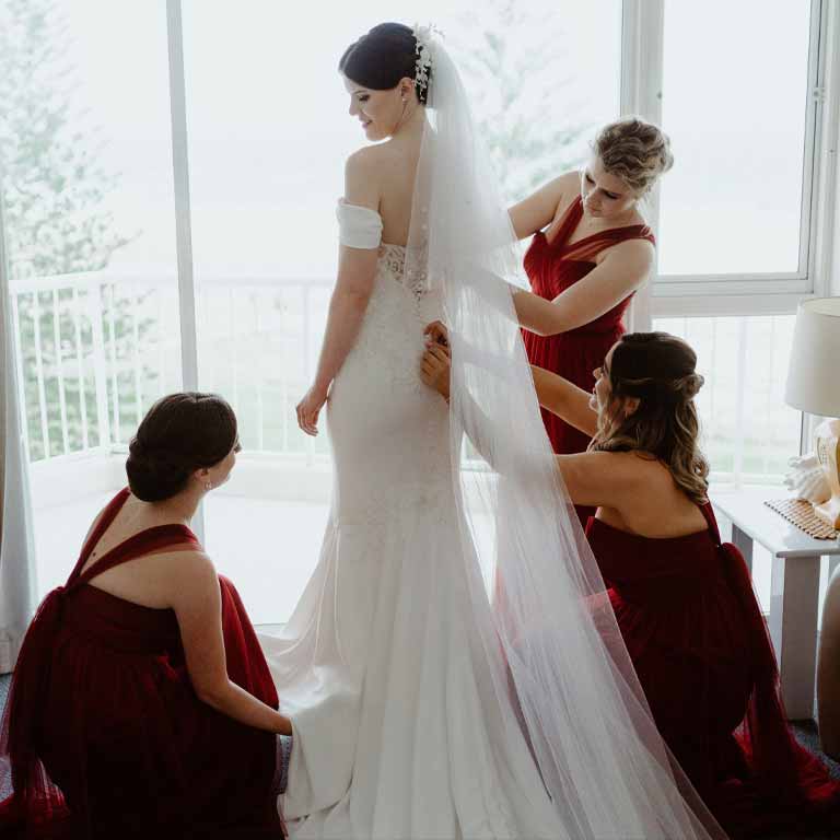 A woman wearing a gown being prepared by red women in a dress for wedding