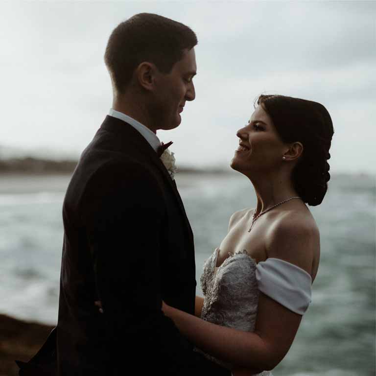 A Bride and a Groom smiling at each other in the beach