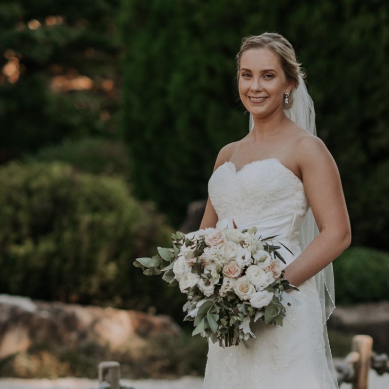 A woman with white gown, holding a bouquet of white roses, standing