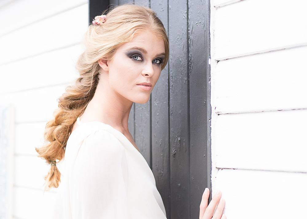 A woman with blonde hair, holding a wall with black door, posing