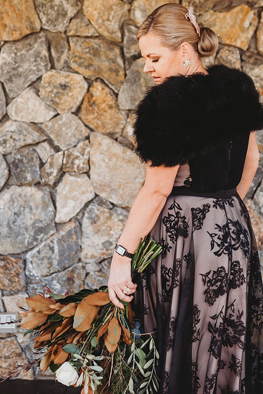 A woman wearing a dark dress, holding a bouquet, facing the back