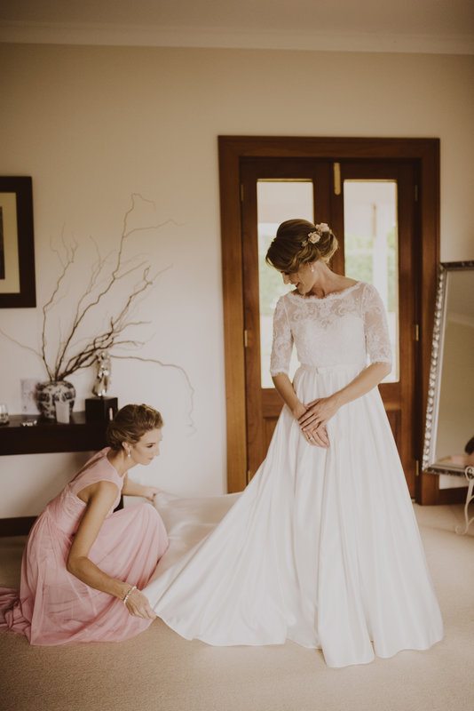 A woman in pink gown, fixing a woman's white gown