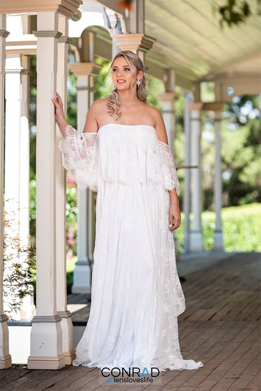 A woman wearing a white long dress, standing next to a post