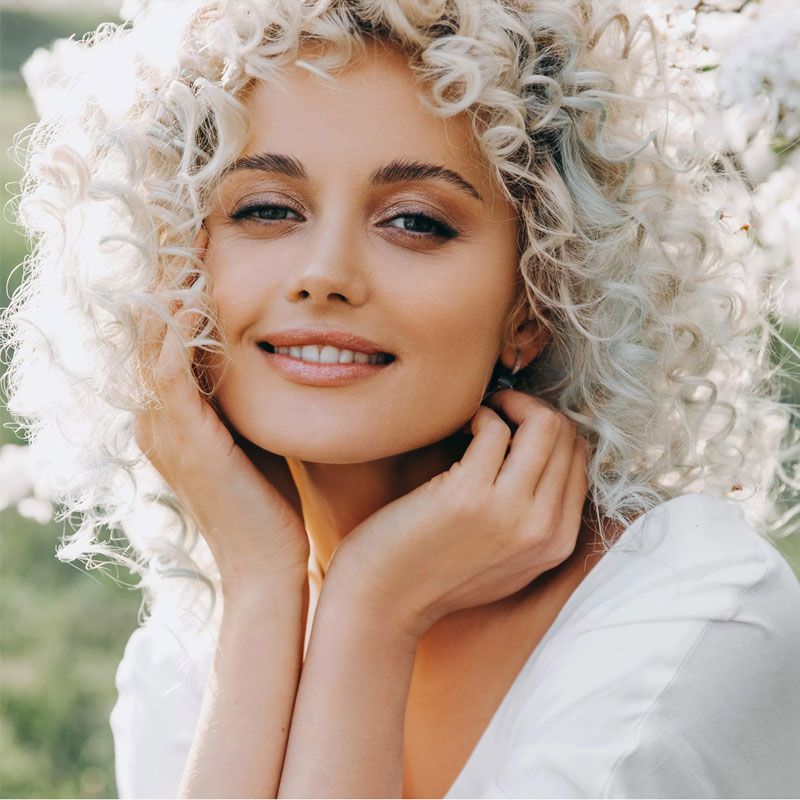 Blonde curly woman in white dress smiling
